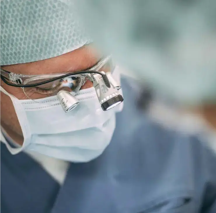 Zahnarzt mit Vergrößerungsbrille und Mundschutz bei einer ästhetischen Zahnbehandlung – Fokus auf die detaillierte Arbeit und Präzision des Arztes.