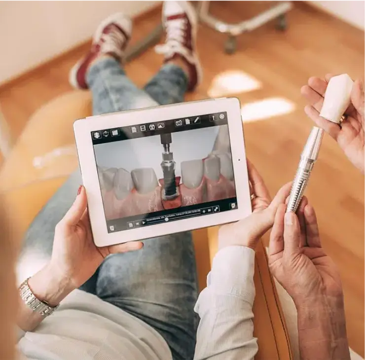 Patient hält ein Zahnimplantat und sieht sich den Behandlungsprozess auf einem Tablet in der Zahnarztpraxis Sandhofpassage Frankfurt an.