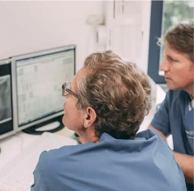Zwei Zahnärzte bei der Analyse von Röntgenbildern auf dem Monitor während der Implantatplanung in der Zahnarztpraxis Sandhofpassage