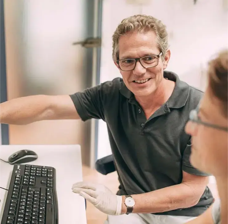 Zahnarzt in der Praxis Sandhofpassage Frankfurt erklärt einer Patientin mit einem Lächeln ihre Zahnimplantatbehandlung.